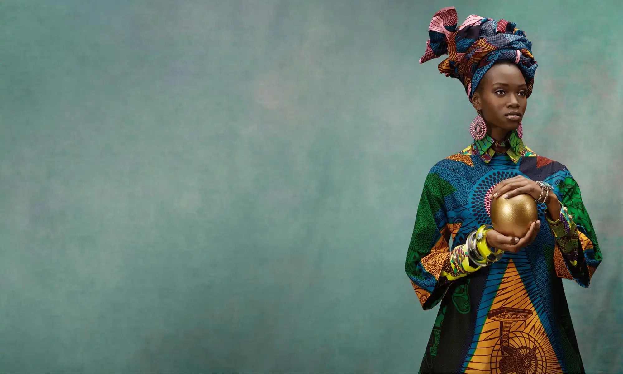 Woman in colorful traditional attire holding a golden sphere against a textured green background