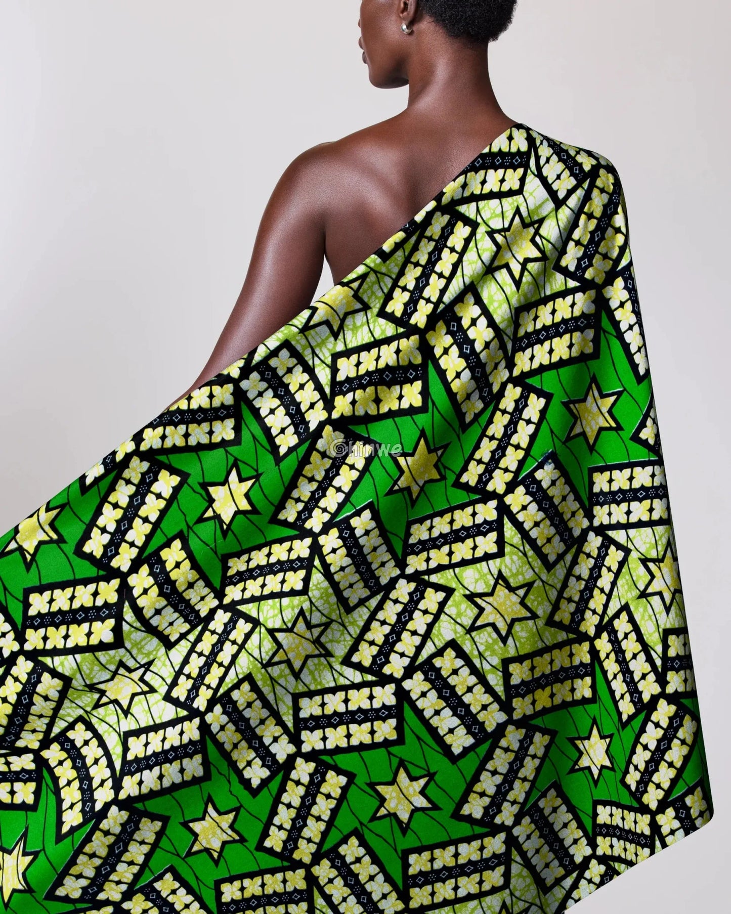 Person draped in a green and yellow patterned fabric with stars on a plain background