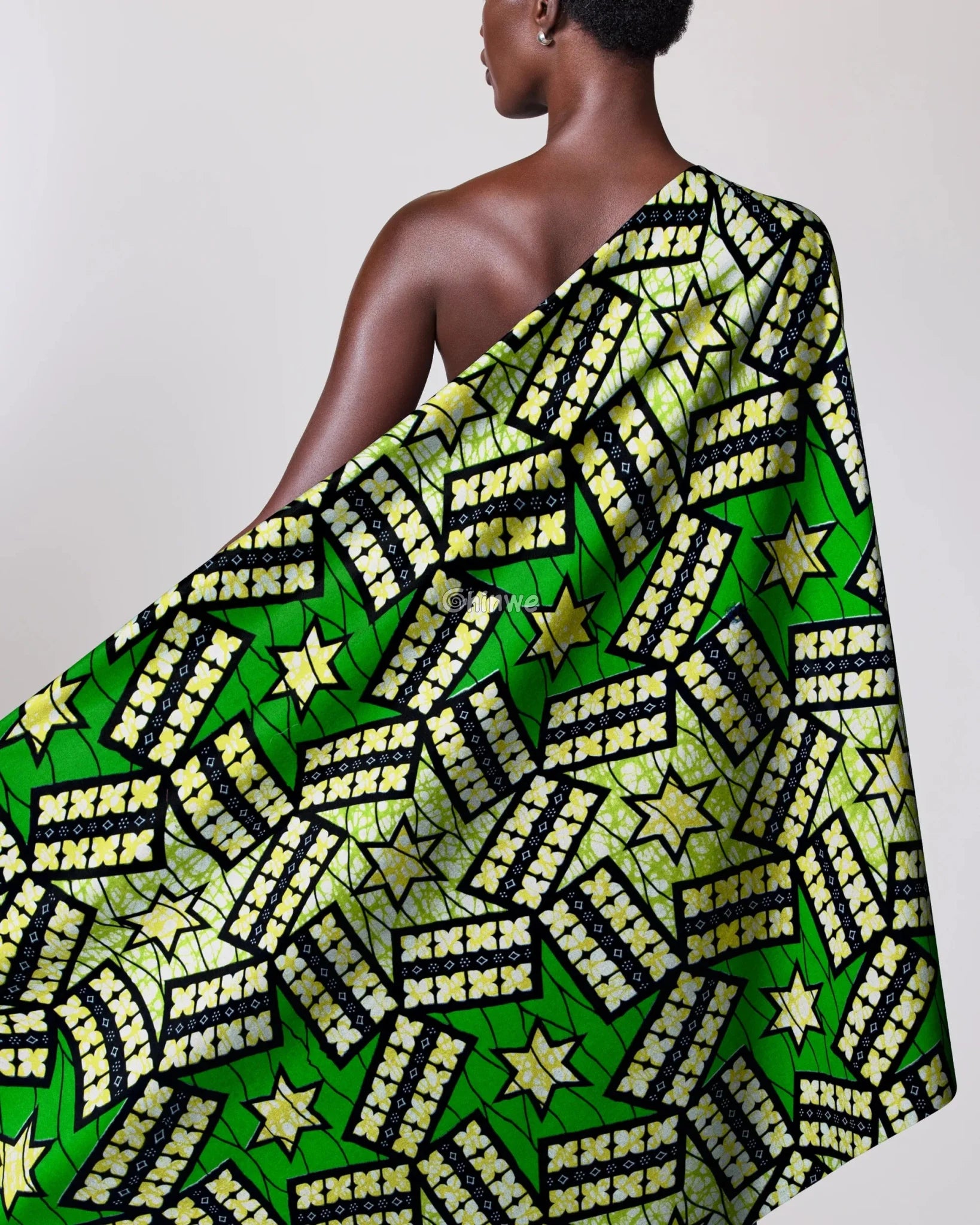 Person draped in a green and yellow patterned fabric with stars on a plain background