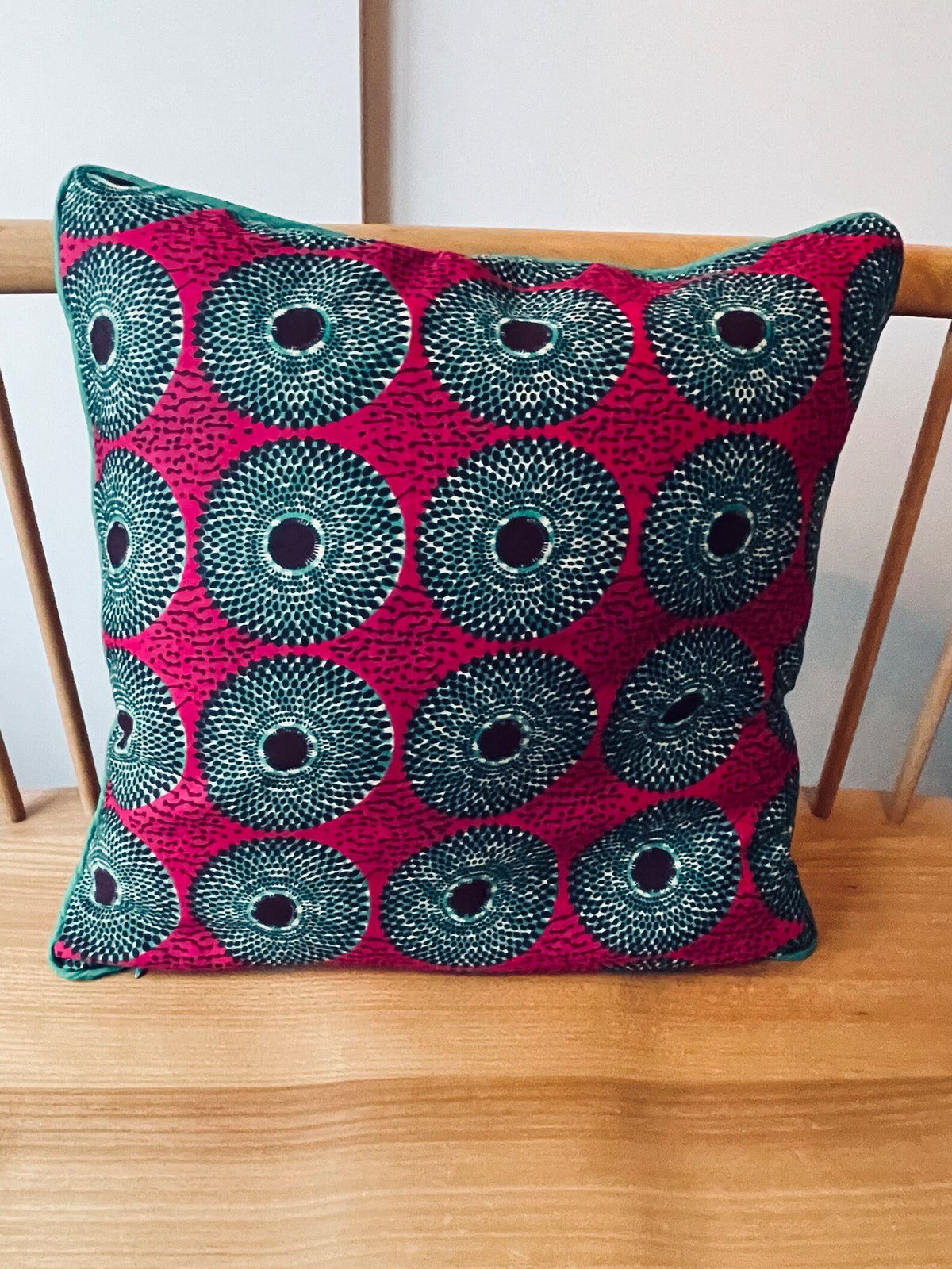 Review image: a pink and teal African-print cushion on a wooden chair.